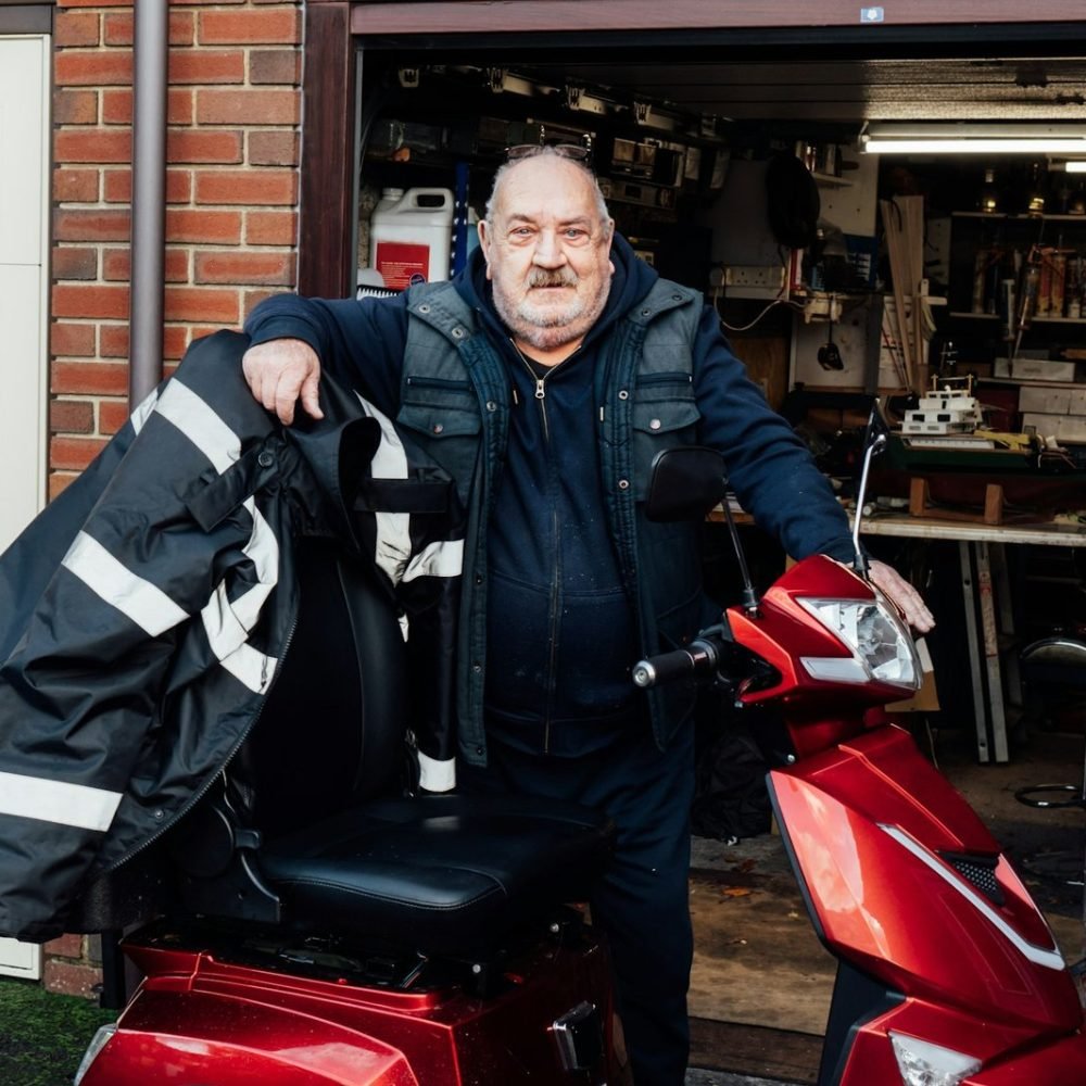 Portrait of elderly man standing near mobility scooter on the background of his garage.